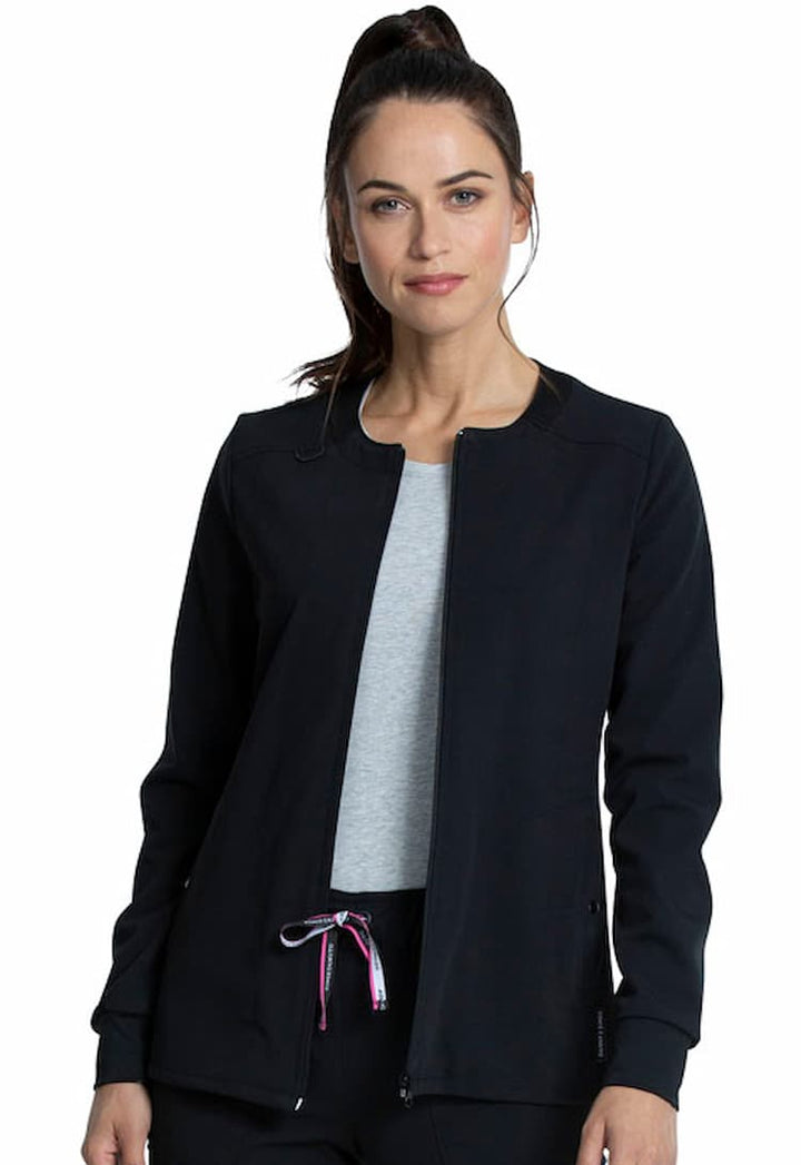 A young female MRI tech wearing a Vince Camuto Women's Zip Front Scrub Jacket in Black size Large featuring knit insets at the neckline & cuffs.