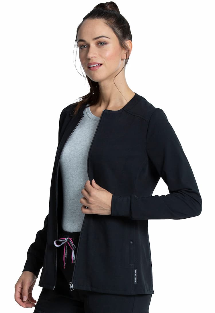 A young female Registered Nurse wearing a Vince Camuto Women's Zip Front Scrub Jacket in Black size XS featuring a round neck & a zip front.
