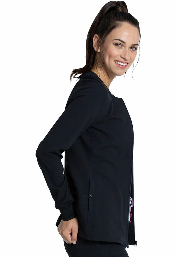 A young female Nurse Practitioner wearing a Vince Camuto Women's Zip Front Scrub Jacket in Black size Medium featuring a bungee ID badge loop on the wearer's right shoulder.