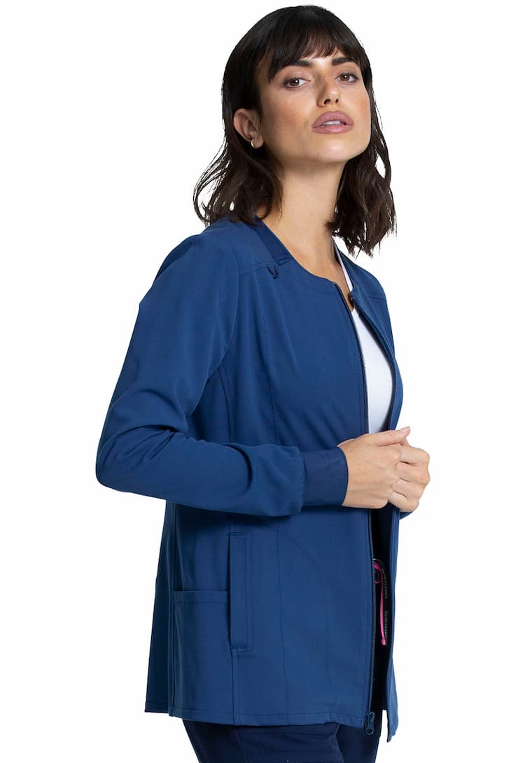 A young female Sonographer wearing a Vince Camuto Women's Zip Front Scrub Jacket in Navy size Medium featuring a bungee ID badge loop on the wearer's right shoulder.