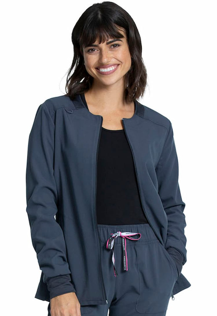 A young female MRI tech wearing a Vince Camuto Women's Zip Front Scrub Jacket in Pewter size Large featuring knit insets at the neckline & cuffs.