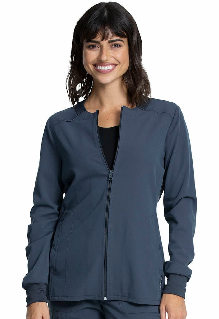 A young female Physician's Assistant wearing a Vince Camuto Women's Zip Front Scrub Jacket in Pewter size 3xl featuring a total of 3 pockets.