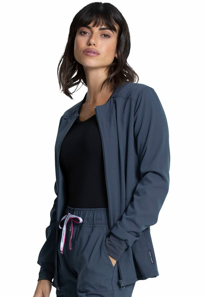 A young female Registered Nurse wearing a Vince Camuto Women's Zip Front Scrub Jacket in Pewter size XS featuring a round neck & a zip front.