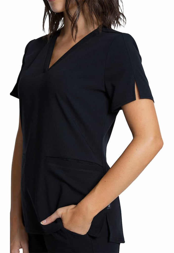 A young female Home Health Aide wearing a Vince Camuto Women's V-neck Scrub Top in Black size 2XL featuring short sleeves with side slits for flair.