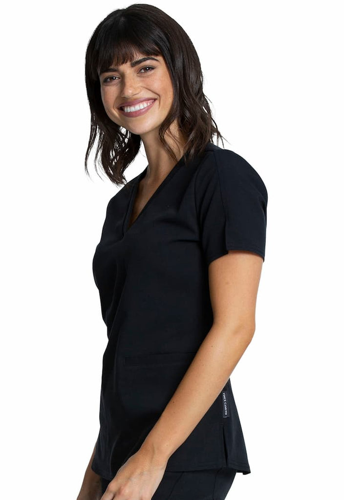 A female Surgical Assistant wearing a Vince Camuto Women's V-neck Scrub Top in Black size Large featuring side slits for additional mobility throughout the day.