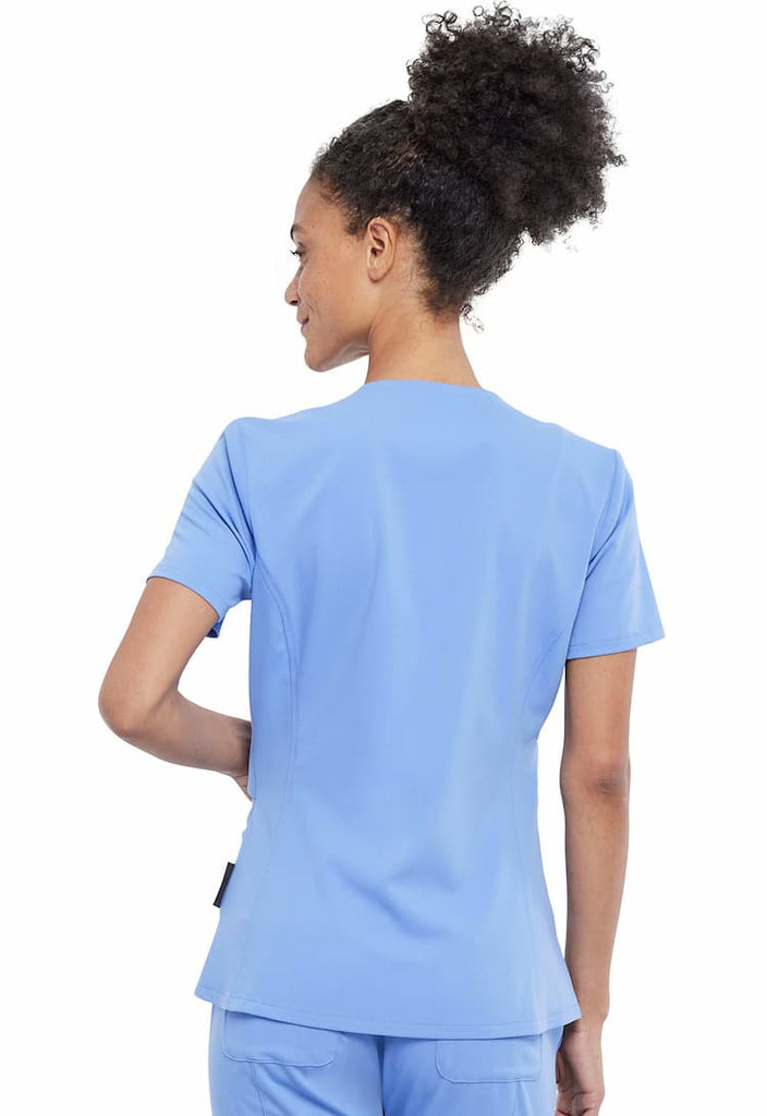 An image of a young female Physical Therapist wearing a Vince Camuto Women's V-Neck Scrub Top in Ceil Blue size Medium featuring a center back length of 26".