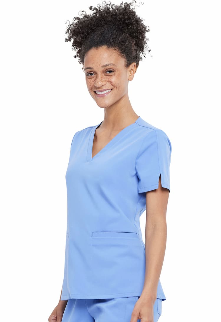 A young female Home Health Aide wearing a Vince Camuto Women's V-neck Scrub Top in Ceil size 2XL featuring short sleeves with side slits for flair.