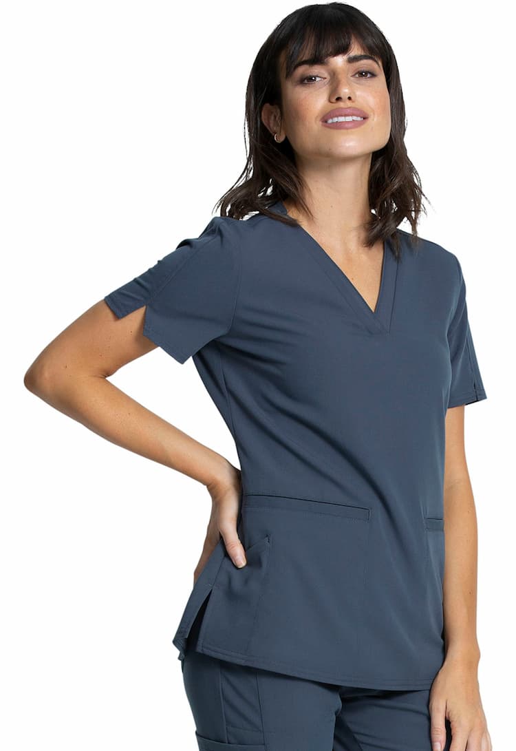 A young female Home Health Aide wearing a Vince Camuto Women's V-neck Scrub Top in Pewter size 2XL featuring short sleeves with side slits for flair.