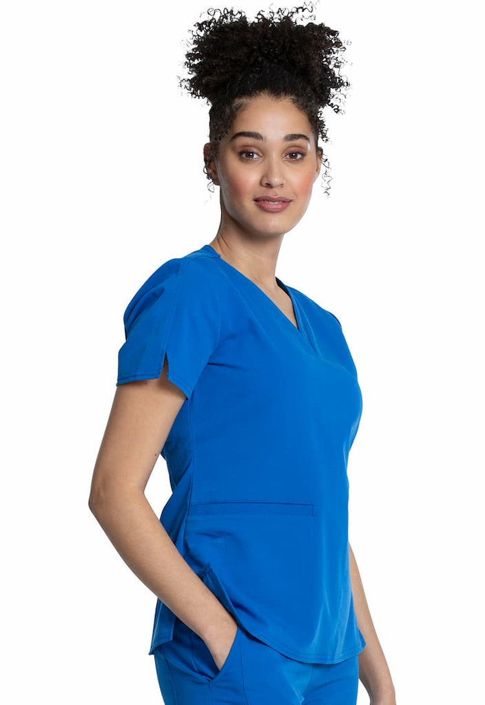 A young female Home Health Aide wearing a Vince Camuto Women's V-neck Scrub Top in Royal size 2XL featuring short sleeves with side slits for flair.