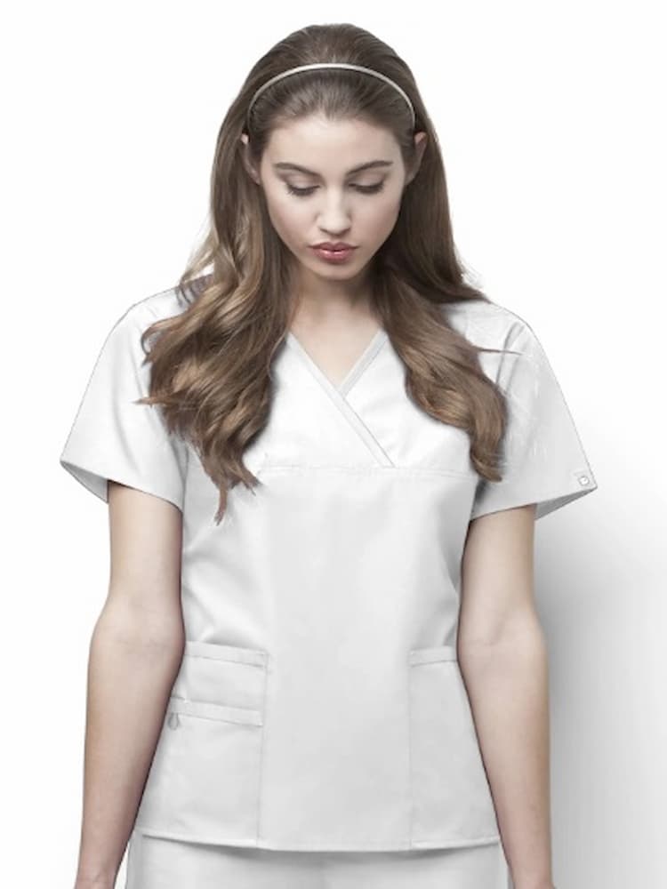 A young female Physician's Assistant wearing a WonderWink Women's Charlie Mock-Wrap Scrub Top in White size XS featuring t wo lower pockets including one WonderWink signature triple pocket with a hidden mesh pocket.