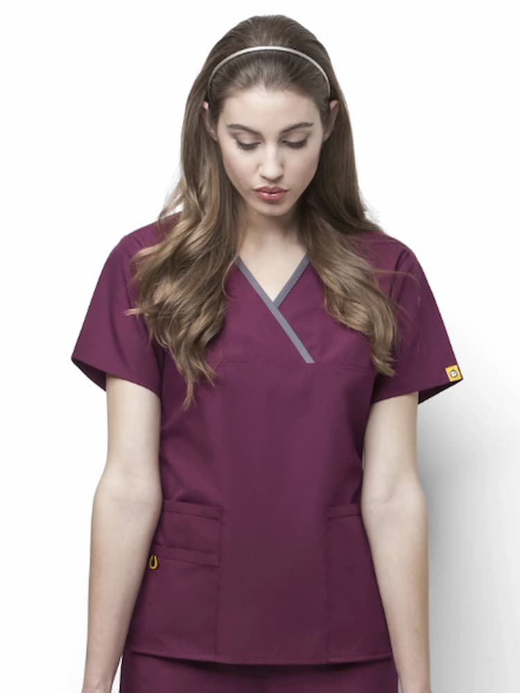 A young female Phlebotomist wearing a WonderWink Origins Women's Charlie Y-neck Scrub Top in Wine 3XL featuring a set-in short sleeves and a total of 5 pockets.