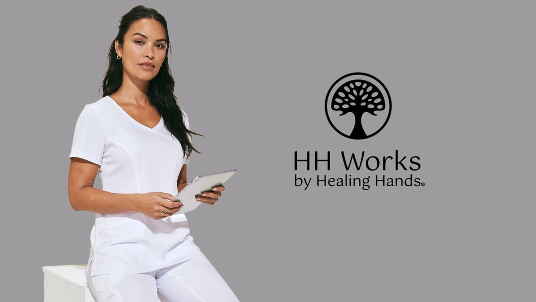 A young female nurse wearing HH Works Scrub in white on a light grey background with the Healing Hands logo to the right.