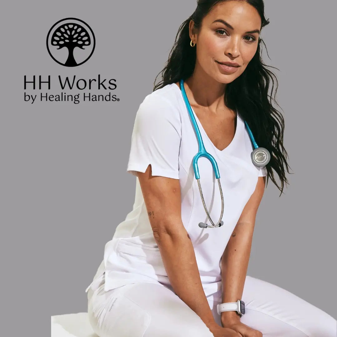 A young female Doctor wearing white scrubs from Healing Hands on a light grey back background featuring the HH Works logo in the top left corner of the image.