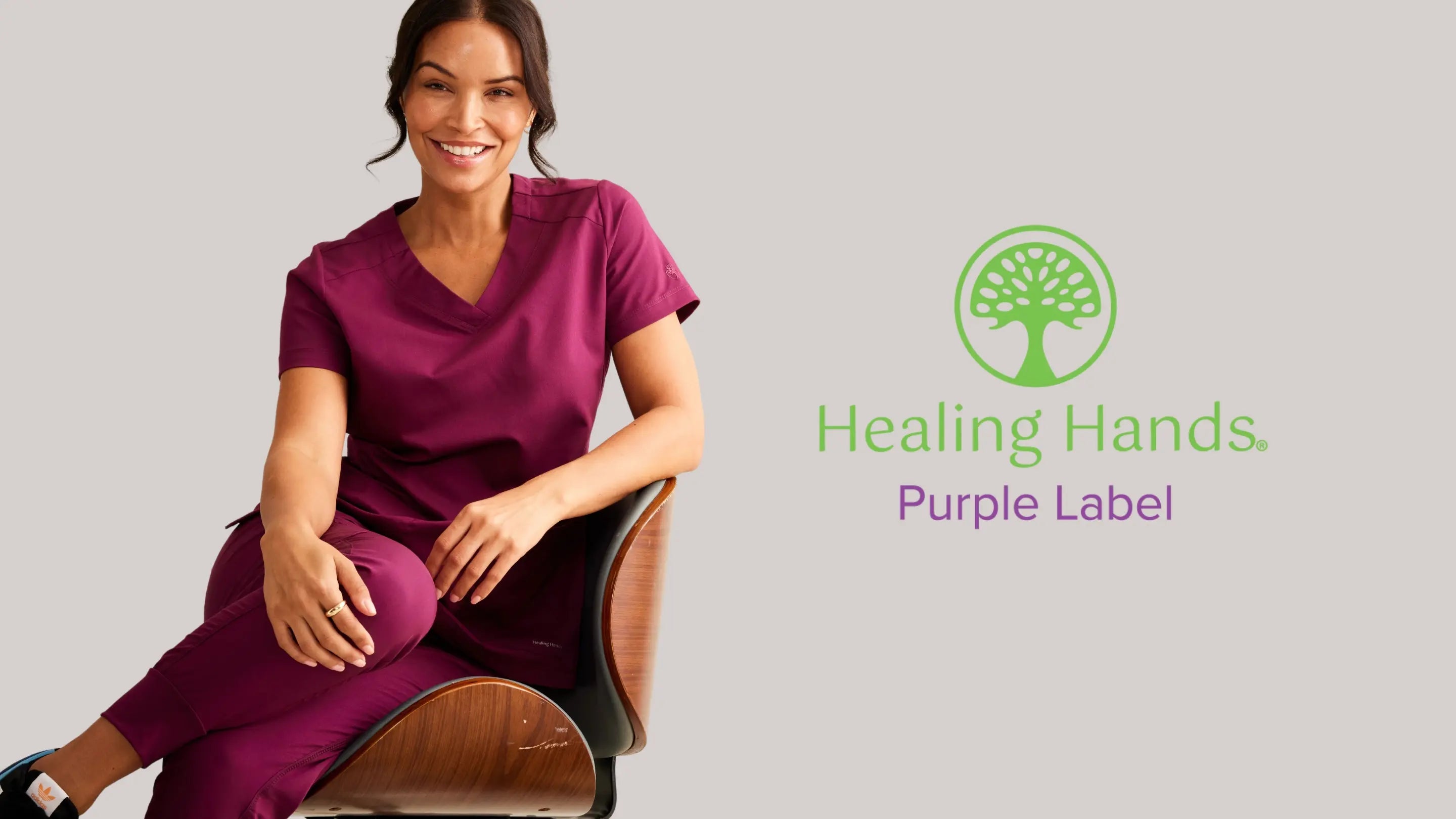 A young female Cardiologist wearing Wine scrubs from Healing Hands Purple Label on a light grey background.