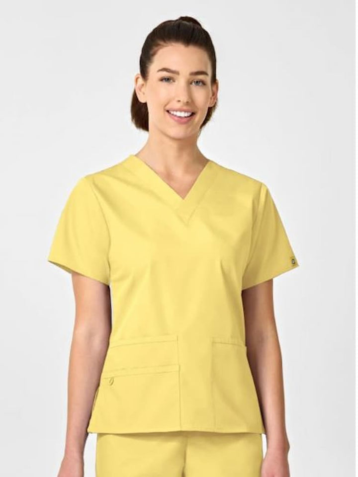 A young female medical assistant wearing a WonderWink Origins Women's Bravo Scrub Top in Yellow size Large featuring short sleeves.