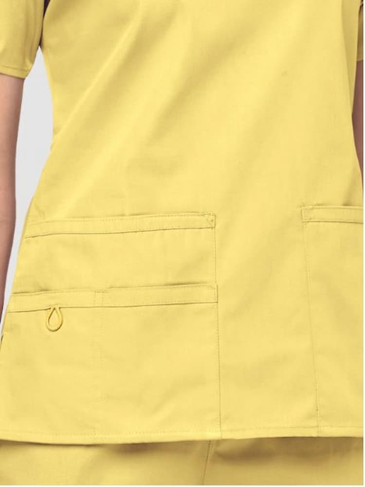 An up close image of the two lower pockets including one WonderWink signature triple pocket with hidden mesh pocket & signature ID bungee loop on the WonderWink Women's Bravo V-neck Scrub Top in yellow.