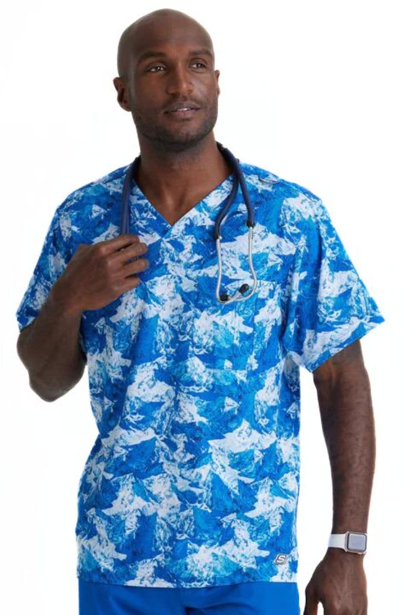 A young male Pediatric Nurse wearing a Skechers Men's Structure Crossover V-neck Scrub Top in "Arctic Landscape" featuring a captivating blend of cool blues, greys, and whites, reminiscent of icy peaks and vast horizons.