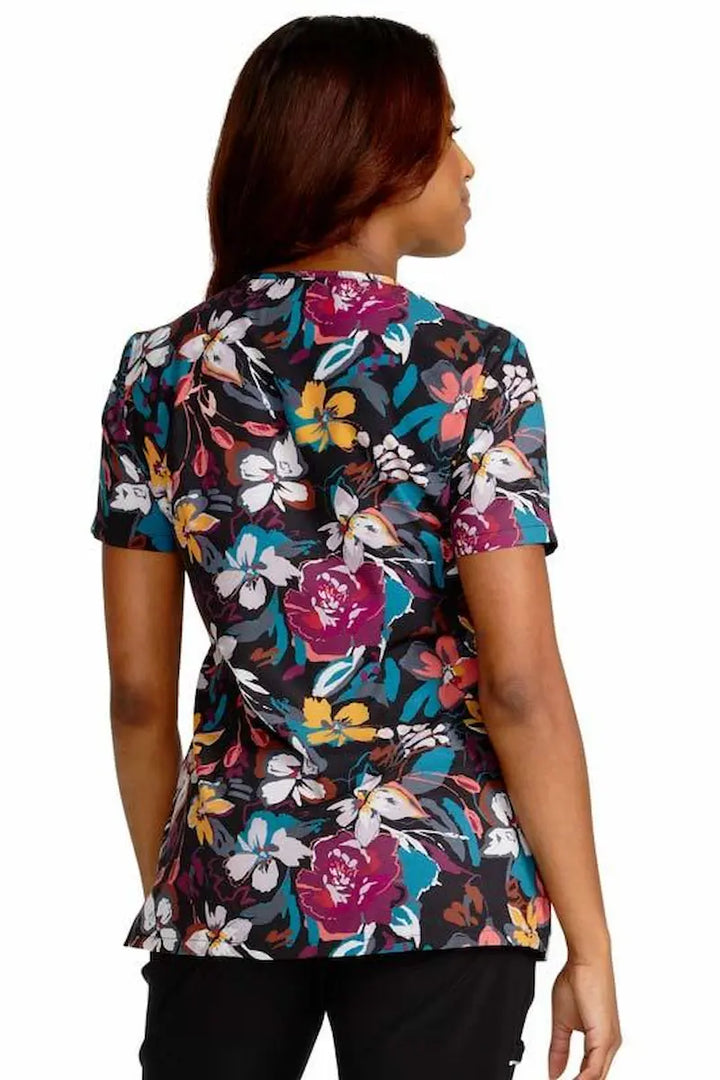 A young female Psychiatric Nurse wearing a Cherokee Women's V-Neck Printed Scrub Top in Artful Blooms featuring a center back length of 26".