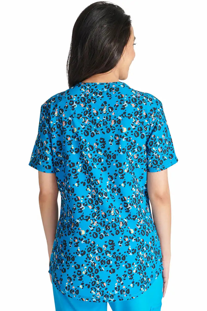 An image of the back of a young female labor and delivery nurse wearing a Cherokee Women's Mock Wrap Scrub Top in "Leopard Pops" size Medium featuring a center back length of 26".