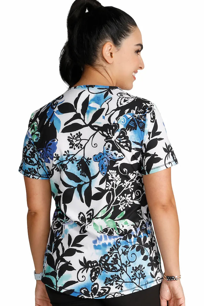 An image of the back of a young female Labor and Delivery Nurse in "Brushy Botanical" size Large featuring a center back length of 26" for optimal coverage.