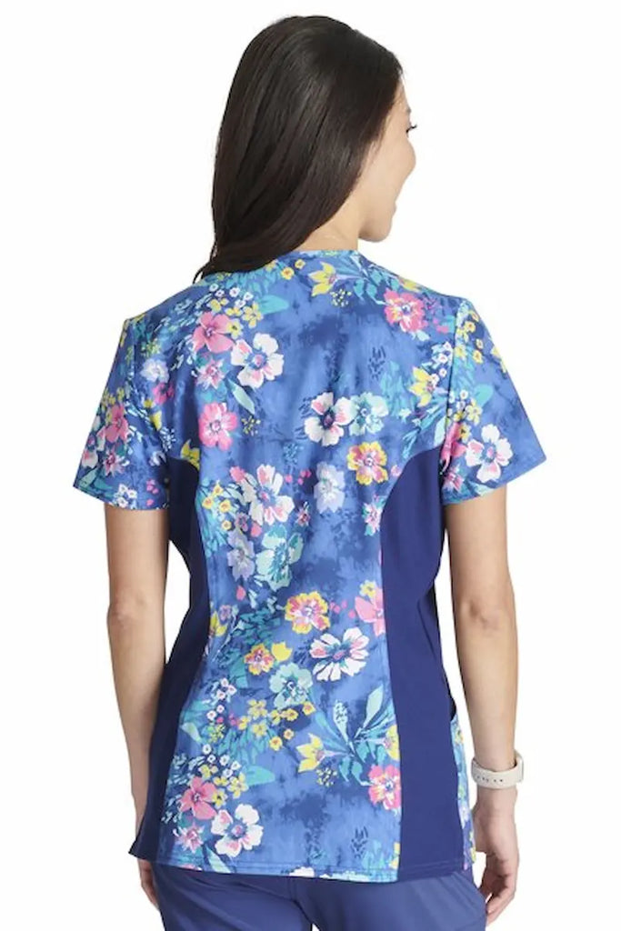 An image of the back of a young female Pediatric Nurse wearing a Cherokee Women's Knit Panel Printed Scrub Top in "Blooming Tie Dye" size Medium featuring a center back length of 26" for optimal coverage.