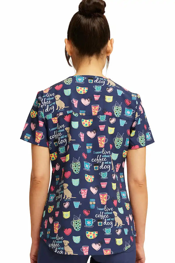 An image of the back of a young female Pediatric Nurse wearing a Cherokee Women's V-neck Printed Scrub Top in "Coffee and My Dog" size Medium featuring a center back length of 26" for optimal coverage.