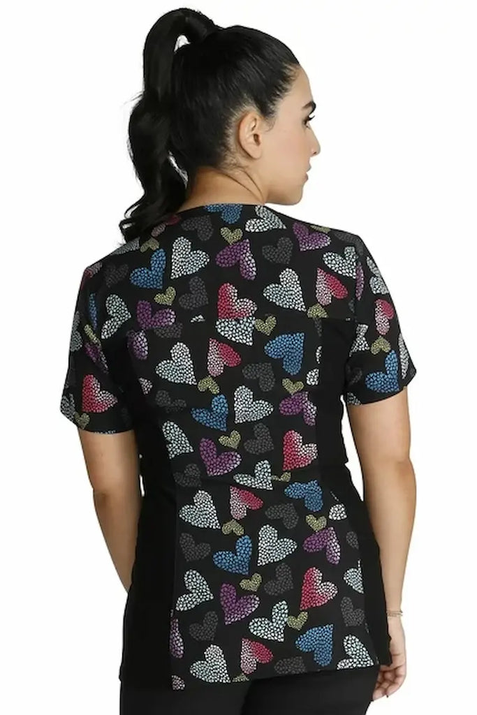 A young female Pediatric Nurse wearing a Cherokee iFlex Women's Knit Panel Printed Scrub Top in "Loving Glow" size Medium featuring a center back length of 26".