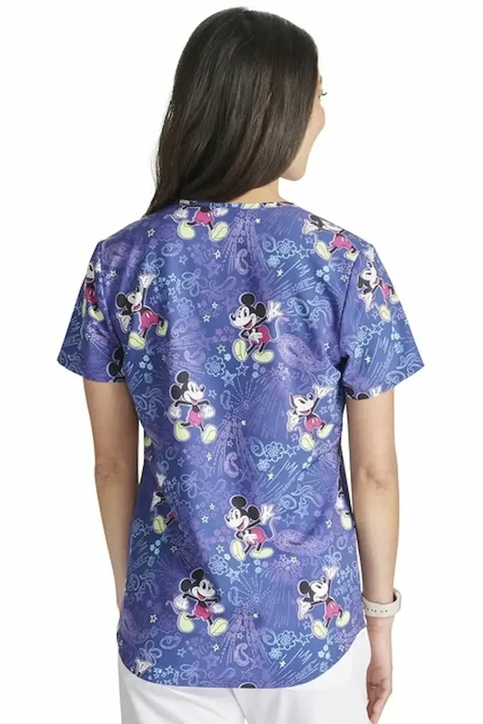 An image of the back of a young female Labor & Delivery Nurse wearing a Tooniforms Women's Printed Scrub Top in "Mickey's Bandana Land" featuring a center back length of 26" for optimal coverage.