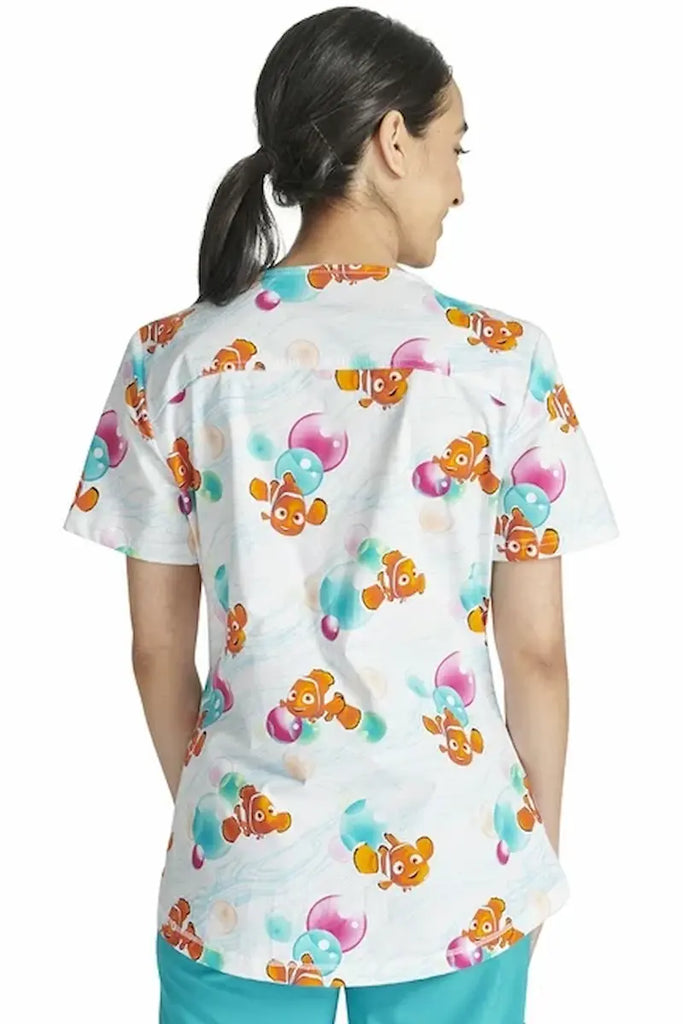 An image of the back of a young female Psychiatric Nurse wearing a Tooniforms Women's V-neck Printed Scrub Top in "Nemo Bubbles" size XL featuring back princess seams for a flattering all day figure. 