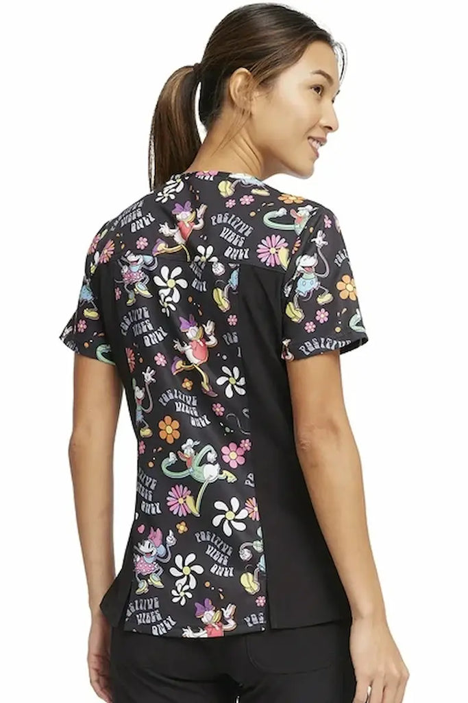 An image of the back of a young female Neonatal Nurse wearing a Tooniforms Women's V-neck Printed Scrub Top in "Positive Vibes" size Medium featuring contrast side panels for a flattering figure.