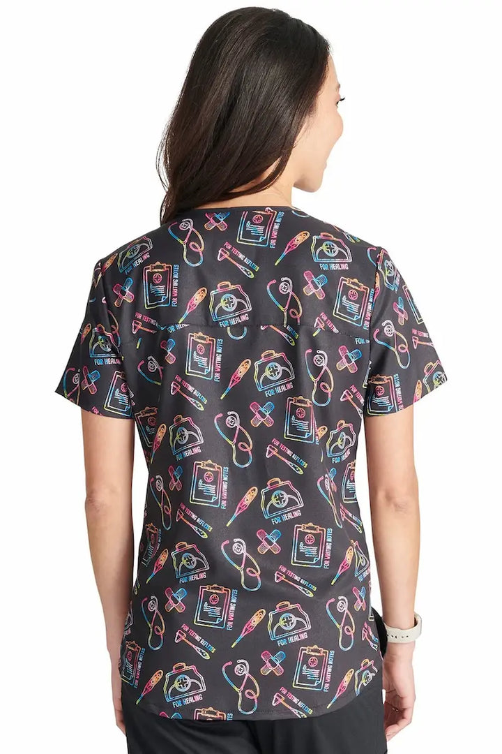 A young female nurse showcasing the back of the Cherokee Women's Printed Scrub Top in Caring Essentials featuring a center back length of approximately 26".