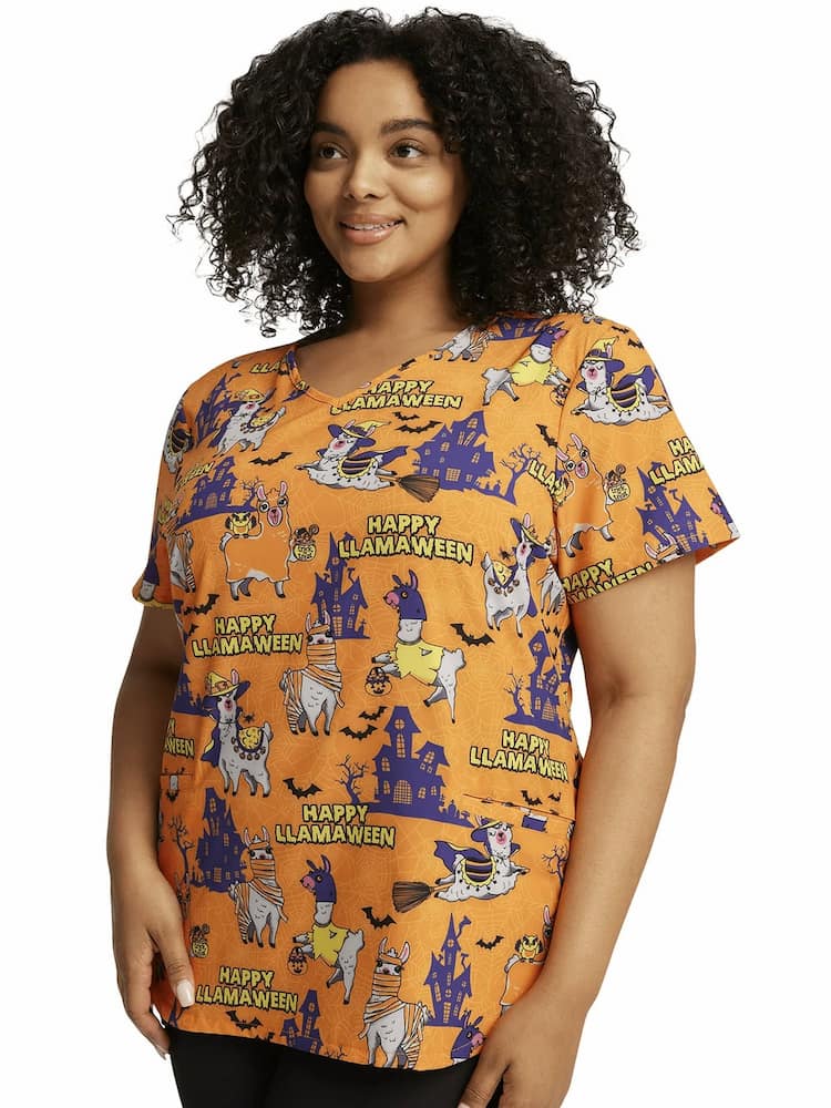 A young female Nurse Practitioner Cherokee Women's V-Neck Halloween Print Scrub Top in "Happy Llamaween" featuring a banded v-neckline.