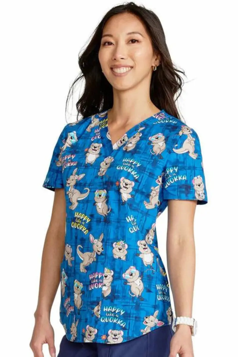 A young female Pediatric Nurse displaying the left side of the Happy as a Quokka Cherokee Women's V-Neck Print Scrub Top on a solid white background.