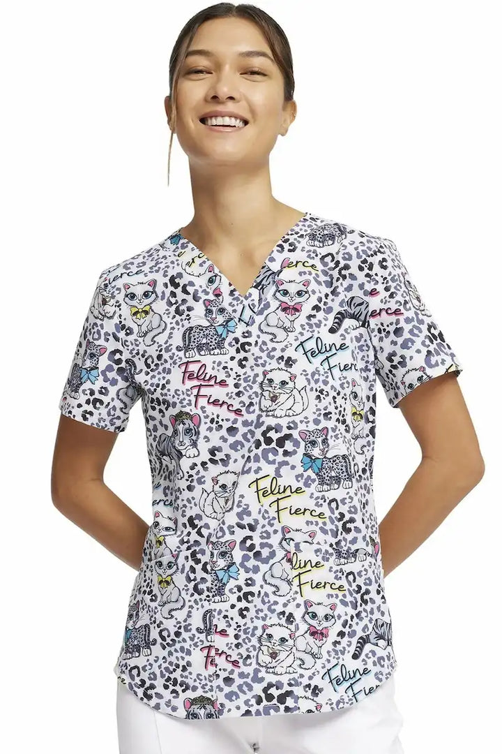 A young female Pediatric Nurse wearing the "Feline Fierce" Cherokee Women's V-Neck Print Scrub Top on a solid white background.