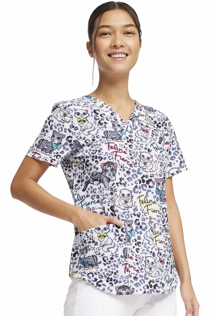 A young female children's nurse showcasing the right side of the "Feline Fierce" Cherokee Women's V-Neck Print Scrub Top featuring a v-neckline and short sleeves.