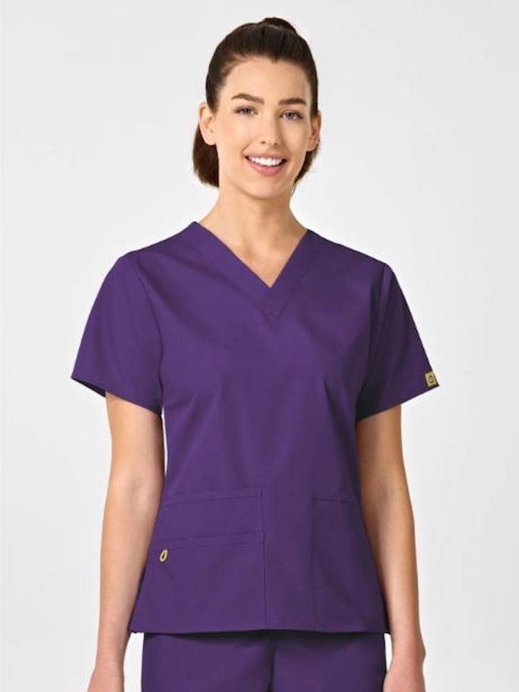 A young female Healthcare Worker wearing a WonderWink Origins Women's Bravo Scrub Top in Eggplant size XS featuring a modern fit.