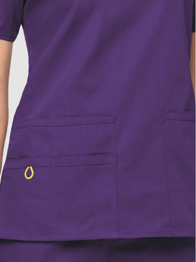 A close up image of the two lower pockets including one WonderWink signature triple pocket with hidden mesh pocket & signature ID bungee loop on the WonderWink Origins Women's Bravo Scrub Top in Eggplant size XL.