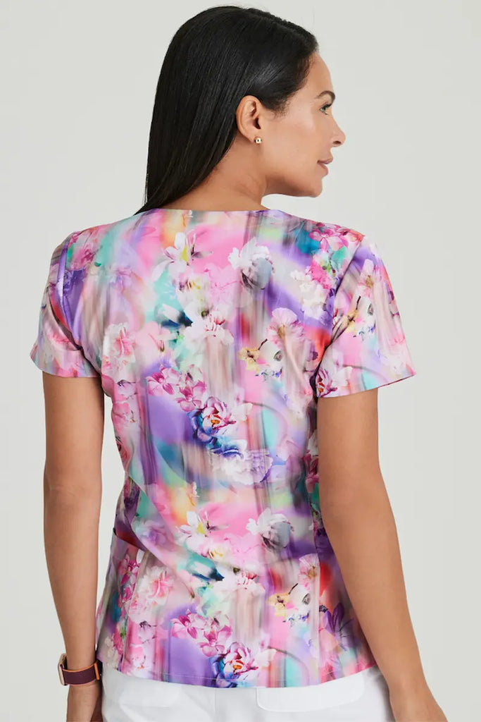 A young female nurse showcasing the back of the Barco One Women's Print  V-neck Scrub Top in Floral Blooms size medium featuring a center back length oof 27.75".