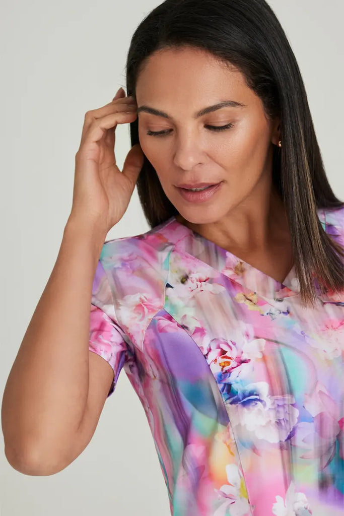 A female Oncologist wearing a Barco One Women's Print V-neck Scrub Top in Floral Blooms featuring short sleeves and princess seaming throughout for gentle shaping and a flattering silhouette.