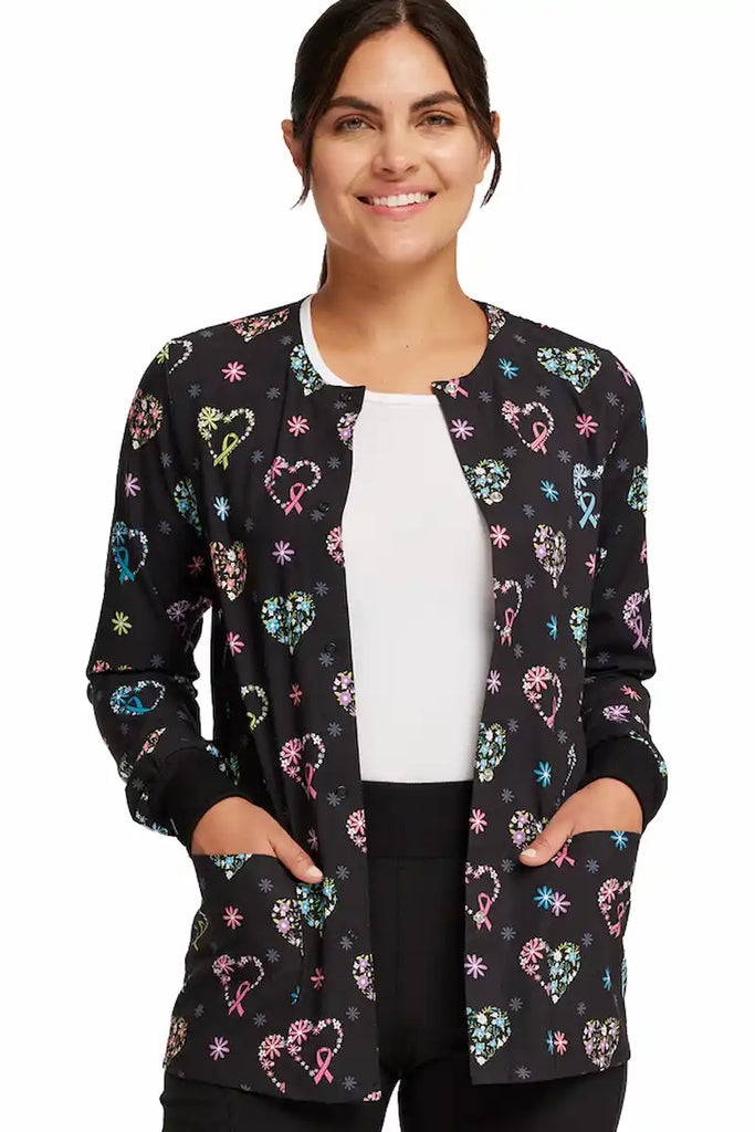 A young female Pediatric Nurse wearing a Cherokee Women's Printed Scrub Jacket in "Care Flor-all" size XS featuring a modern classic fit with snap front closure.