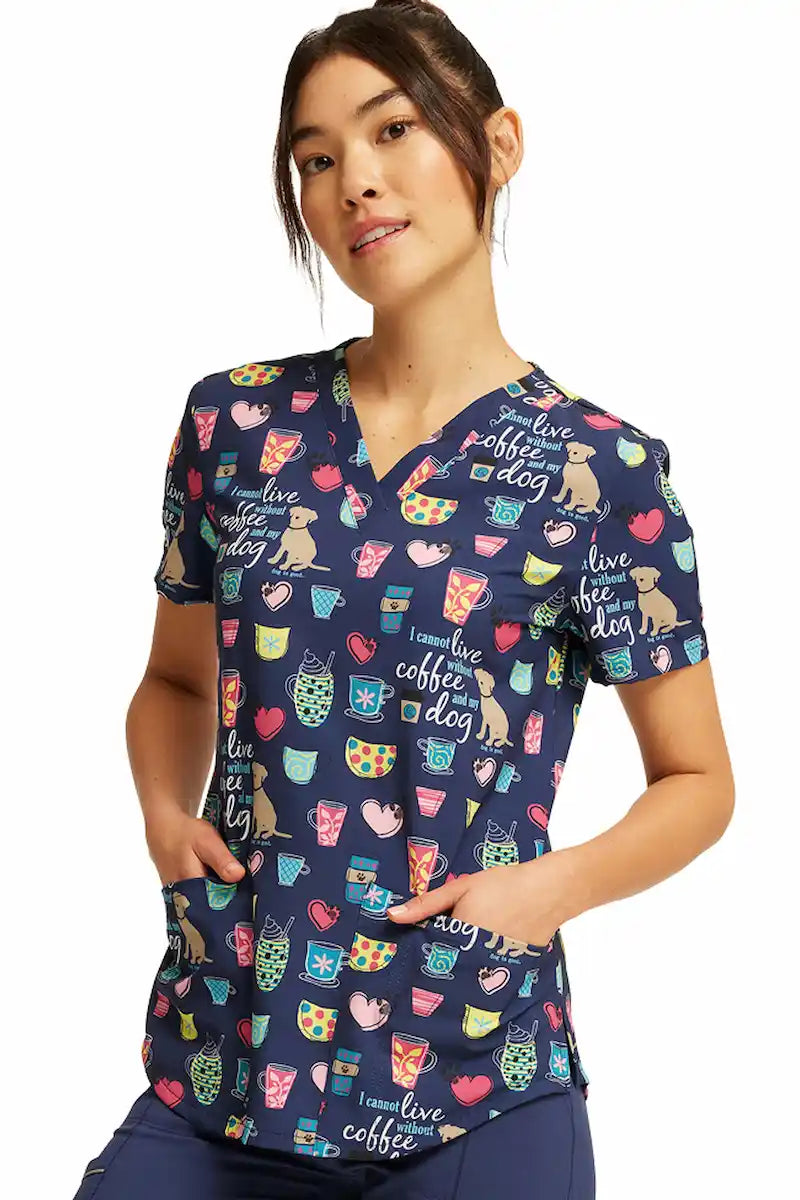 A young female Labor and Delivery Nurse wearing a Cherokee Women's V-neck Printed Scrub Top in "Coffee and My Dog" size Large featuring two front patch pockets.