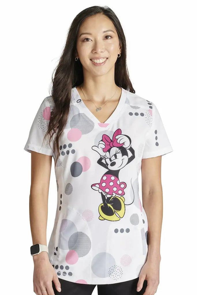 A young female Neonatal nurse wearing a Tooniforms Women's V-neck Printed Scrub Top in "Running in Circles" in size large featuring an The main attraction is the eye-catching print of Minnie Mouse running in circles on a white background with multi-colored polka dots.