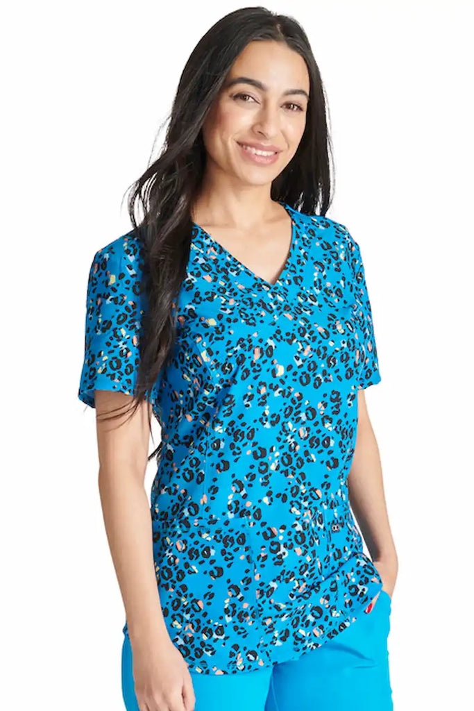 A young female Pediatric Nurse wearing a Cherokee Women's Mock Wrap Printed Scrub Top in "Leopard Pops" size large featuring a contemporary fit.