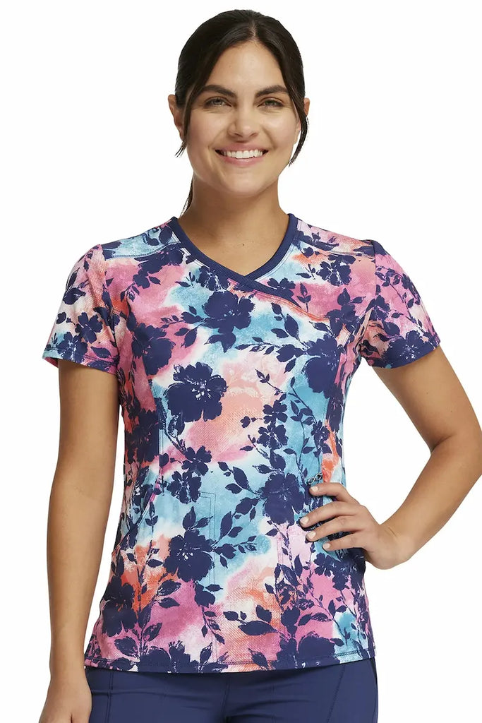 A young female Psychiatric Nurse wearing a Cherokee Infinity Women's Mock Wrap Printed Scrub Top in "Artistic Blooms" size large featuring a modern classic fit.