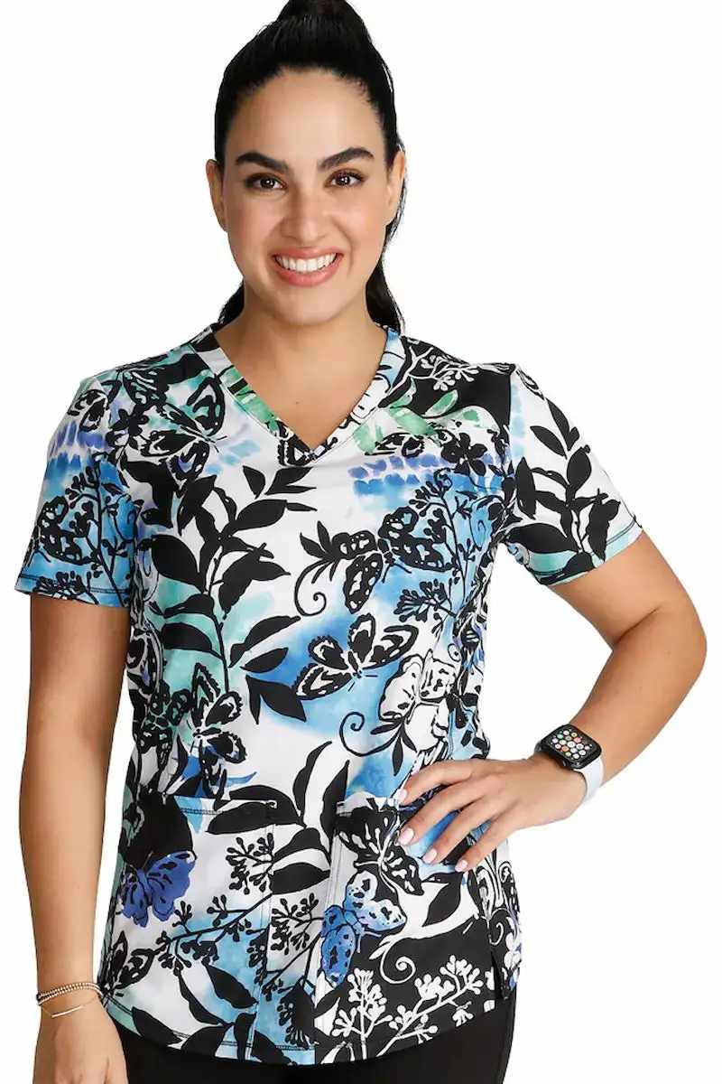 A young female Pediatric Nurse wearing a Cherokee Women's V-neck Printed Scrub Top in "Brushy Botanical" size Medium featuring a contemporary fit.