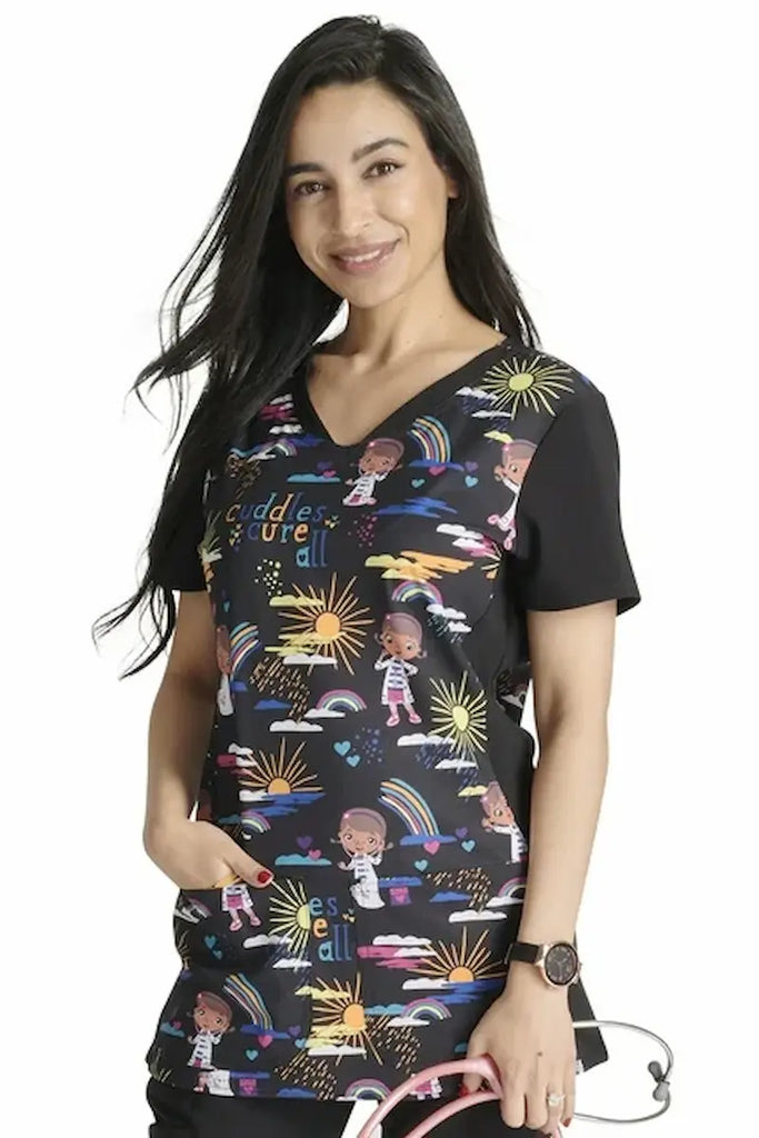 A young female Labor & Delivery Nurse wearing a Tooniforms Women's V-neck Printed Scrub Top in "Cuddles for All" size Large featuring two front patch pockets for ample storage space.
