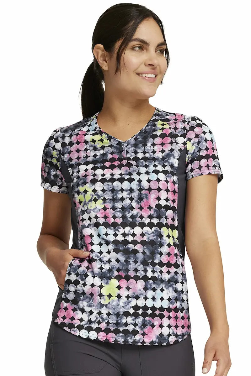 A young female Pediatric Nurse wearing a Cherokee iFlex Women's V-Neck Print Scrub Top in "Dot's So Retro" size XS featuring a modern classic fit.