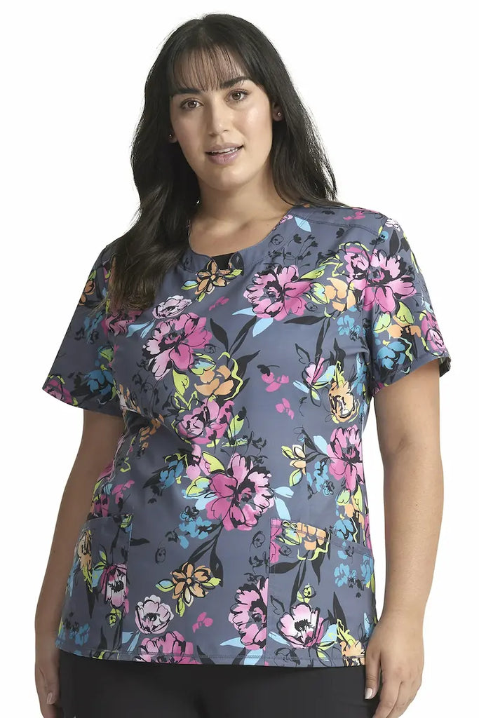 A young female Pediatric Nurse wearing a Cherokee Infinity Women's Round Neck Printed Scrub Top in "Electric Blossoms" size 3XL featuring a modern classic fit.