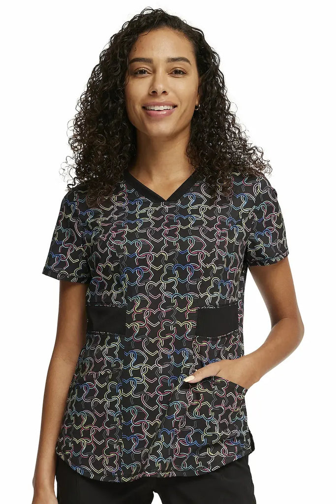 An image of a young female Pediatric Nurse wearing a Cherokee Infinity Women's V-neck Printed Scrub Top in "Links of Love" size medium featuring a modern classic fit.