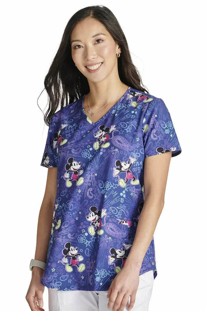 A young female Neonatal Nurse wearing a Tooniforms Women's V-neck Print Scrub Top in "Mickey's Bandana Land"  featuring a modern classic fit.
